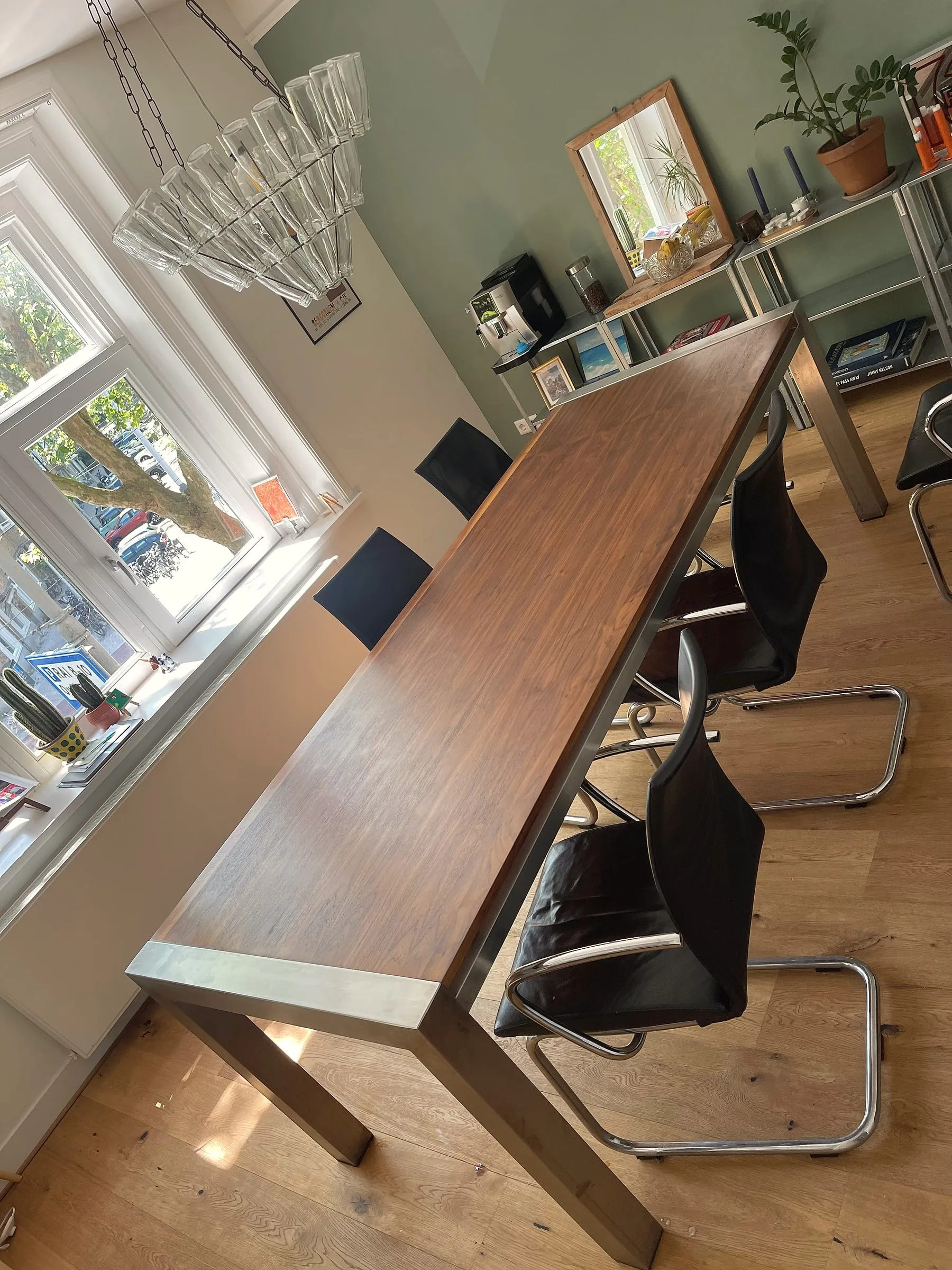 Lange tafel met een donkerhouten blad in een stalen frame, met stoelen aan beide kanten, in een lichte kamer