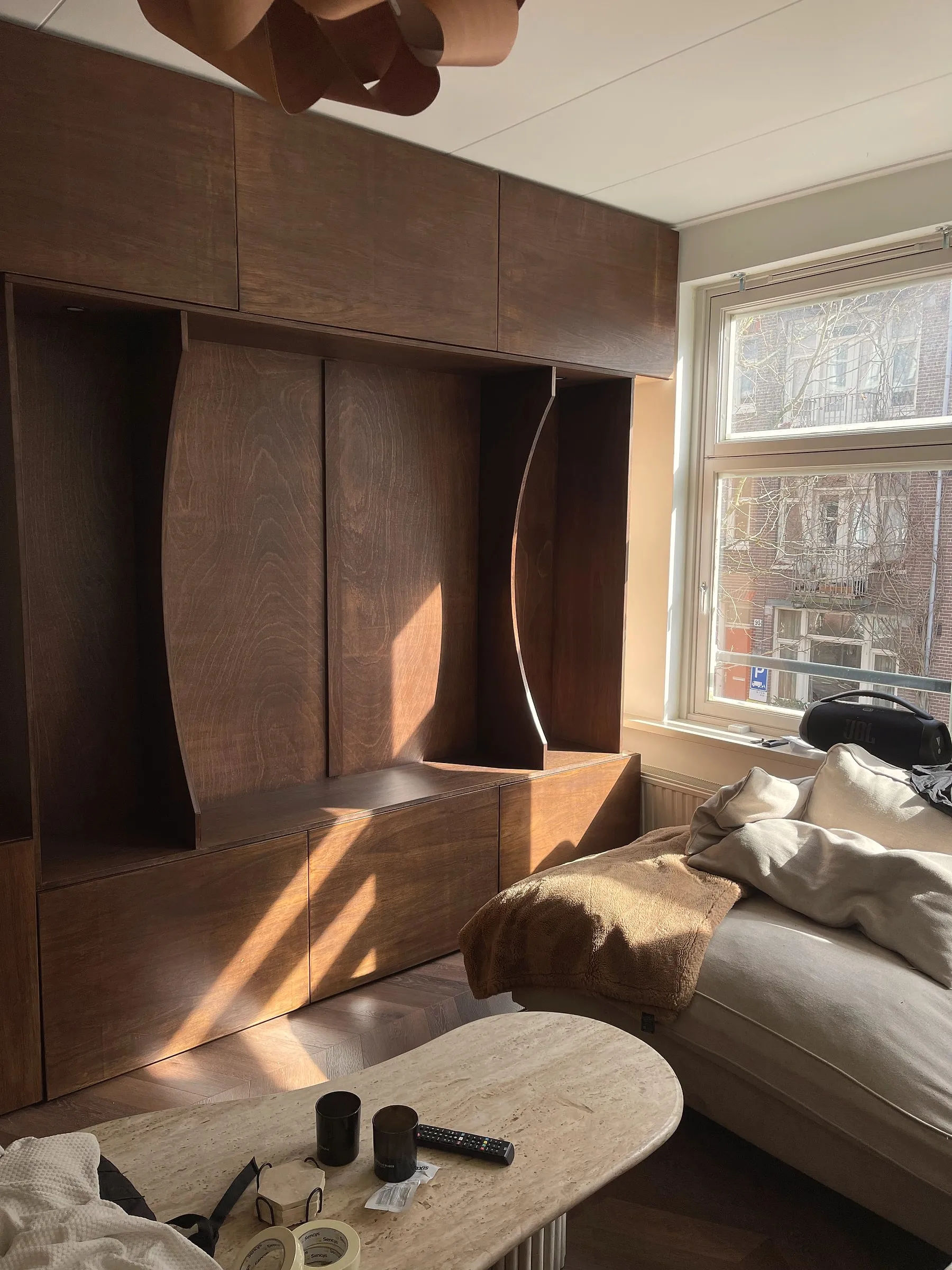 Ingebouwde wandkast op maat in donker hout, met gebogen panelen rond de open nissen, in een zonnige woonkamer
