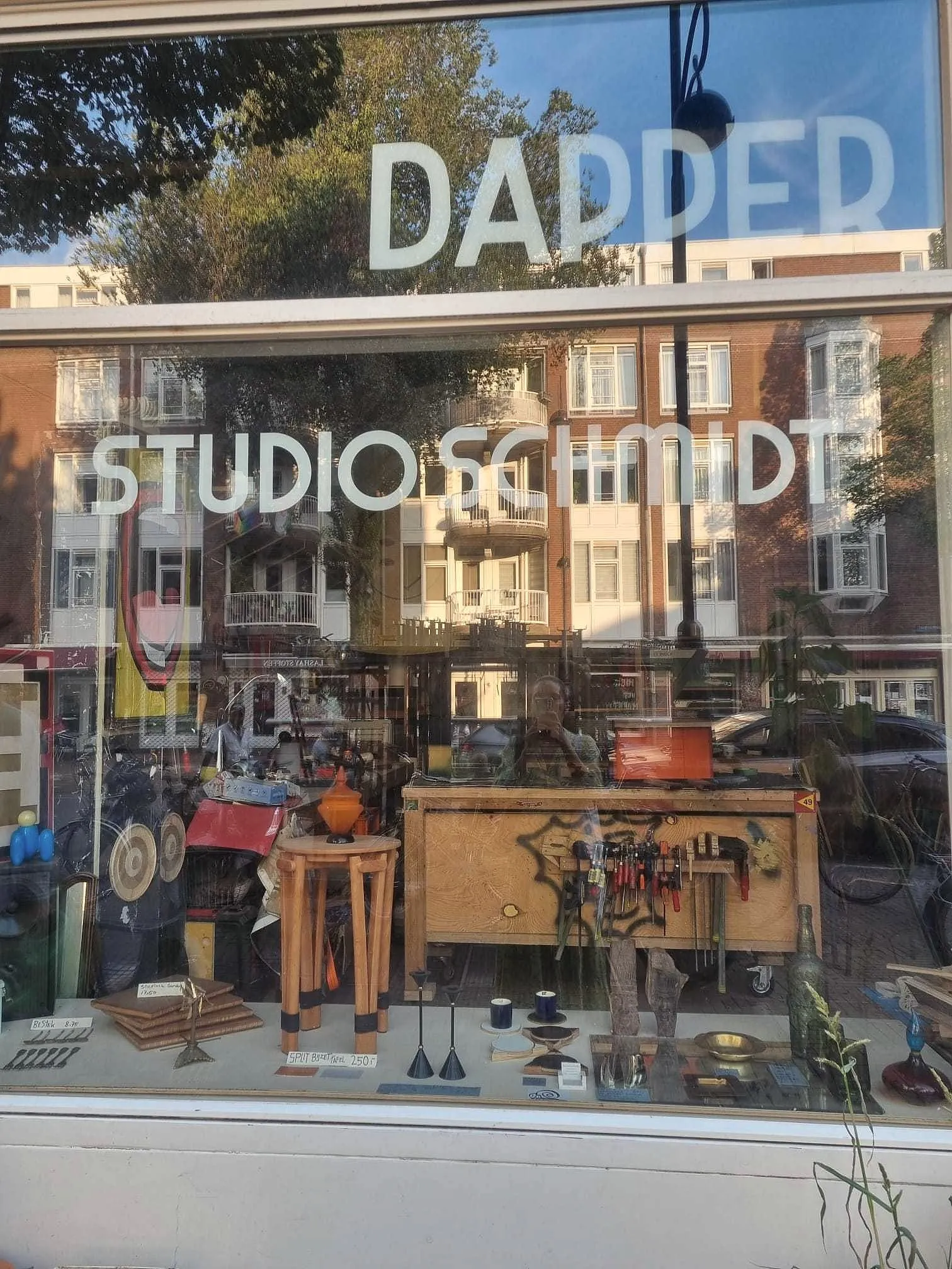 Etalage met de letters DAPPER en STUDIO SCHMIDT, de buurt weerspiegeld in het glas